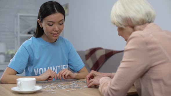 Young Volunteer Helping Aged Woman Playing Puzzle Game in Nursing Home, Care