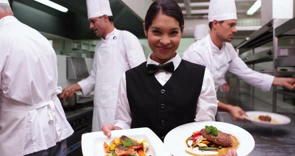 Smiling Waitress Showing Two Dishes to Camera