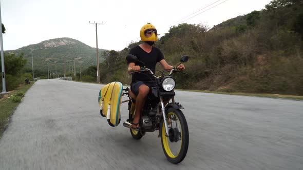 Kitesurfer with surfboard rides motorbike to go kiting, exploring Vietnam coast