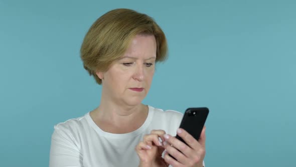 Old Woman Excited for Success While Using Smartphone Isolated on Blue Background