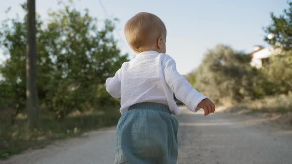 Toddler in White Shirt Walks on Country Road Past Lush Trees