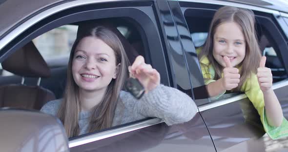 Young Caucasian Woman Bragging Car Keys As Little Girl Showing Thumbs Up From Automobile. Rich