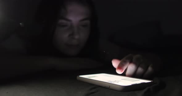 Hand Is Using Smart Phone On Bed At Night. Blurred Woman Is Yawning