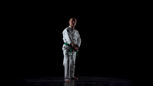 Kendo Fighter on White Kimono Practicing Martial Art with the Bamboo Bokken on Black Background