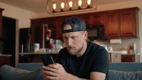 A Young Man is Sitting at Home on the Couch and Playing Video Games on His Phone