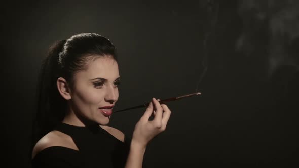 Beautiful Woman Smokes a Cigarette in a Mouthpiece on a Black Background