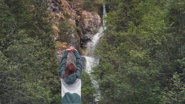 Happy Young Redhaired Woman Raises His Hands Near the Waterfall in the Dolomites Mountains