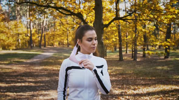 Young Female in Sportswear is Standing in Autumn Forest Taking Off Protective Mask Smiling and