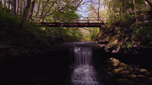 Backwards drone flight from foot trail bridge over waterfalls