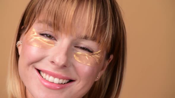 Beautiful Smiling Woman with Short Hair in Gold Eye Patches Looking in Camera and Smiling Over