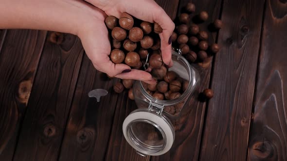 Closeup of a Woman Pouring a Macadamia Nut Into a Jar on a Wooden Background