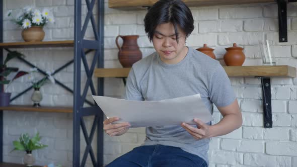 Stressed Nervous Asian Young Man Throwing Away Business Graph Sitting on Kitchen Countertop