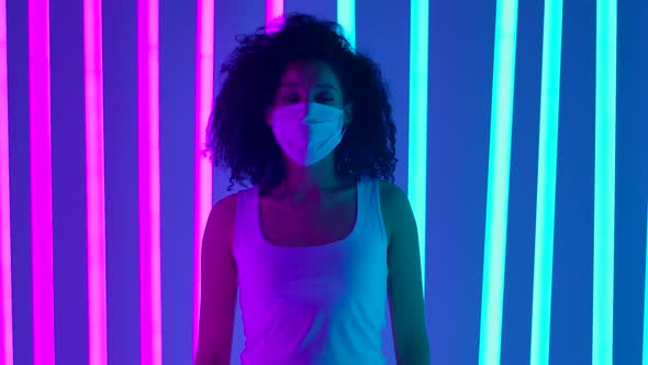 A African American Woman in a Medical Protective Mask in the Studio Against the Background of Neon