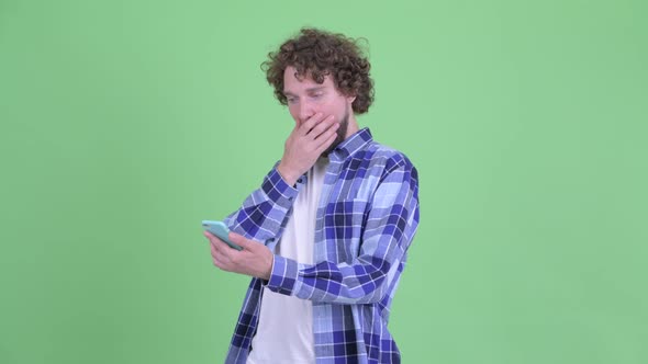 Happy Young Bearded Hipster Man Using Phone and Looking Surprised