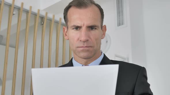 Pensive Middle Aged Businessman Reading Documents in Office Paperwork