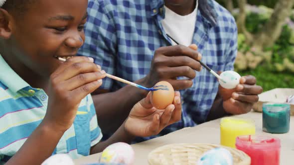 Animation of happy african american father and son painting easter eggs together in garden