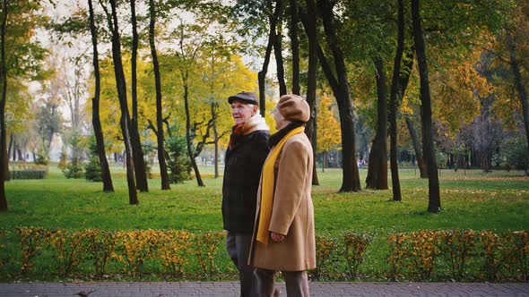 Retired Grandparents in Elegant Warm Outerwear are Holding Hands Talking and Smiling During Walk in