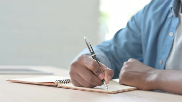 Close Up of Young African Man Writing on Notebook