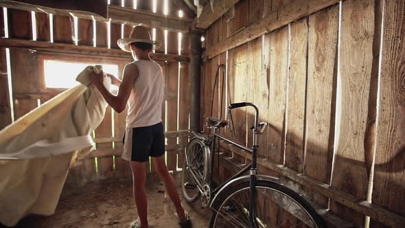 Adolescent Country Boy in Straw Hat Taking Off the Cover From Vintage Bicycle and Rolling It Out of