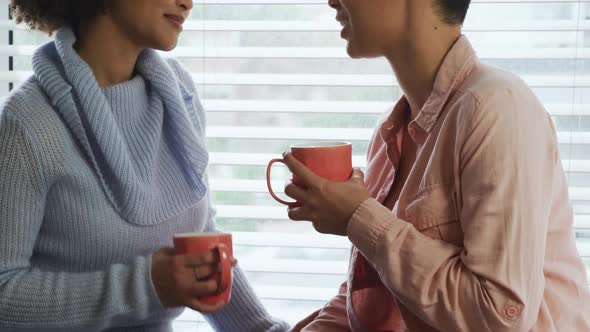 Lesbian couple having coffee sitting on window sill