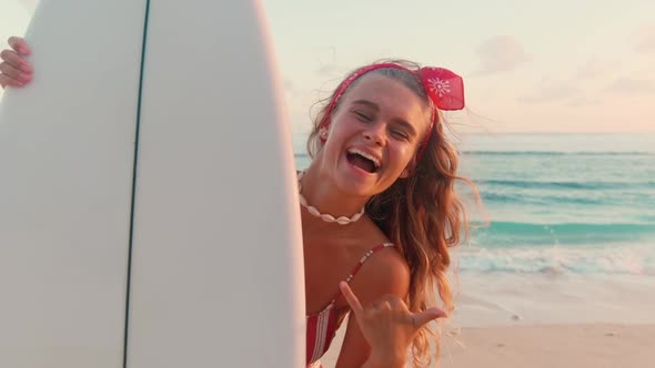 Young Caucasian Woman Sends Greetings to Friends Surfers Showing Shaka Gesture