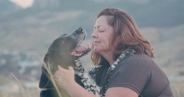 A Plump Woman Hugs Her Spotted Dog Against the Backdrop of a Mountain Landscape