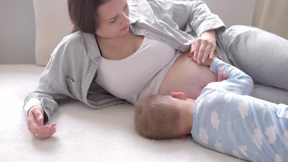 Close Up Happy Pregnant Woman with Little Baby Son Touching Her Tummy in Bed at Home