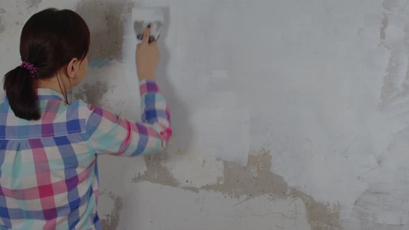 A Woman Puts Putty on the Walls While Making Repairs in Her House