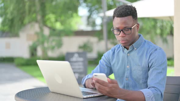 Attractive African Man Using Smartphone in Outdoor Cafe