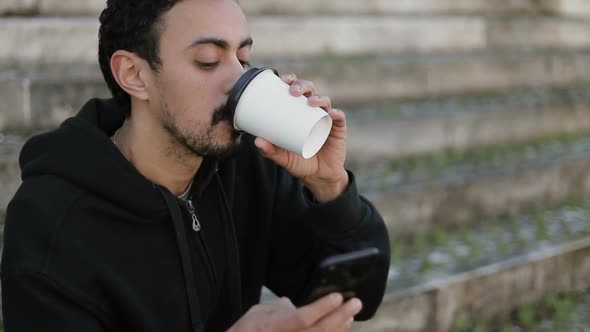 Young Arabic Man Texting on Phone, Drinking Takeaway Coffee 