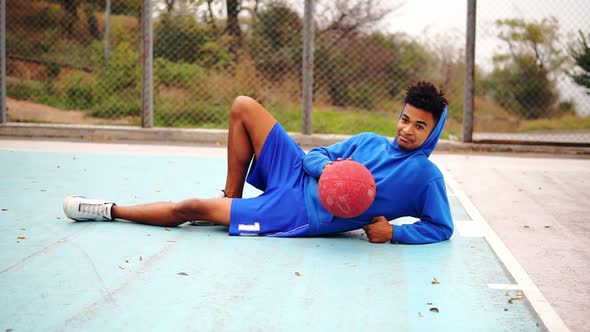 Young African American Laying on the Floor of the Playing Field and Playing with Basketball Ball
