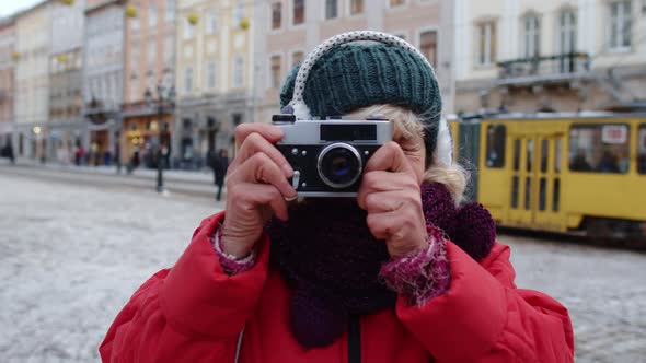 Senior Old Woman Tourist Taking Pictures with Photo Camera Using Retro Device in Winter City Center