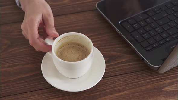 A Woman Works With A Computer At Home And Drinks Coffee. A Laptop And A White Cup Of Coffee
