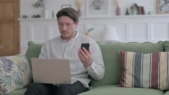 Man with Laptop using Smartphone on Sofa