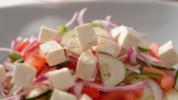 Camera follows putting diced feta cheese over salad. Slow Motion.