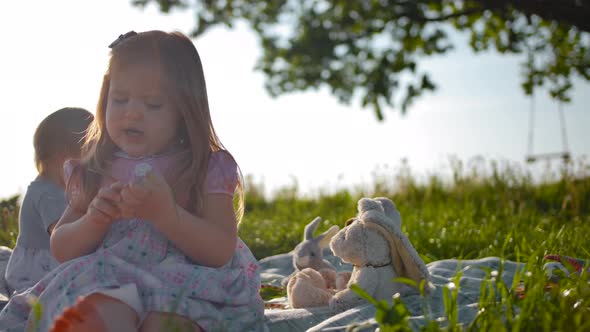 Two Little Girls Are Sitting on a Picnic Cover in the Middle of a Large Green Meadow