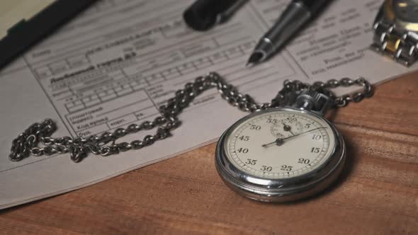 Vintage Stopwatch Lies on Wooden Desk with Old Documents and Counts Seconds