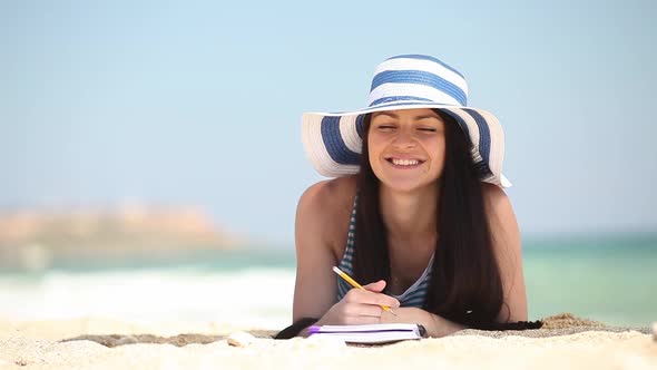 Young female student lying on sand with note and book on the beach