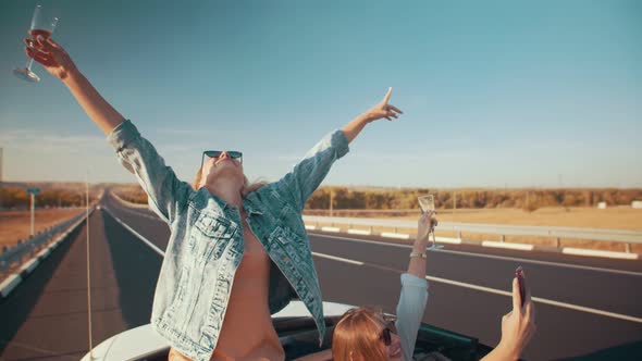 Two Young Beautiful Women on a Cabriolet with a Cabriolet Top Drink Champagne and Have Fun During