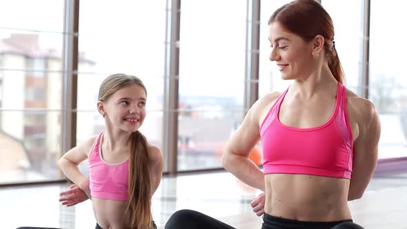 Mom and daughter train in the gym. The daughter repeats her mother's movements