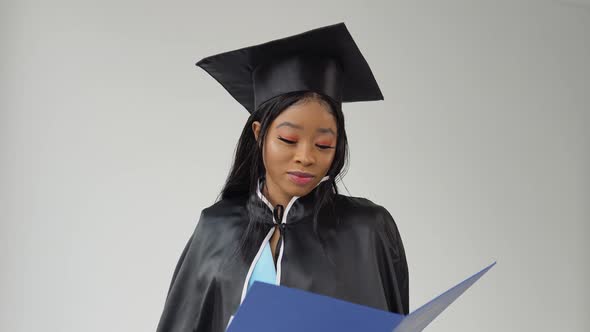 African American Female Graduate in a Classic Suit and Mantle of a Master Stands with a Diploma in