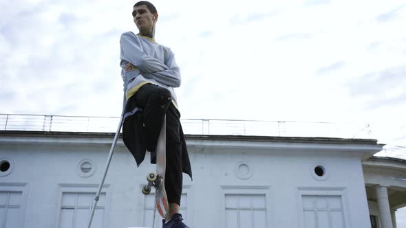 Handsome Young Man with One Leg on Crutches Training with Skateboard