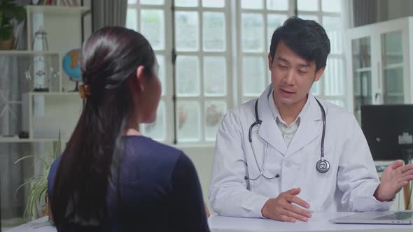 Asian Man Doctor Is Talking With Young Female Patient During Consultation In A Health Clinic