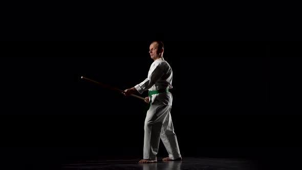 Kendo Fighter on White Kimono Practicing Martial Art with the Bamboo Bokken on Black Background.