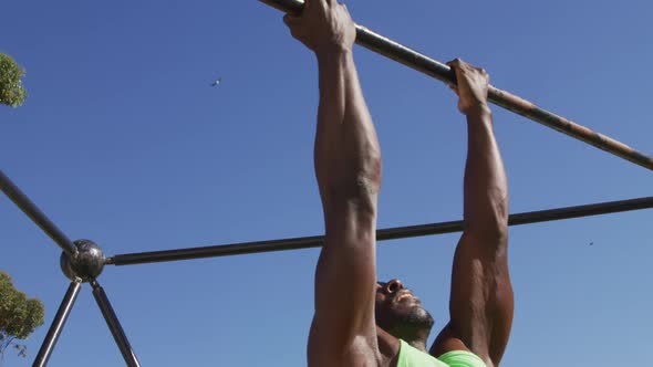 Fit african american man exercising outside, doing chin-ups on a climbing frame