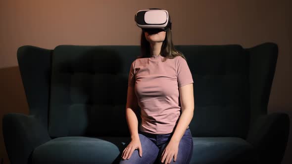 Woman Is Sitting on Sofa in Virtual Reality Glasses and Touching Hands in Air