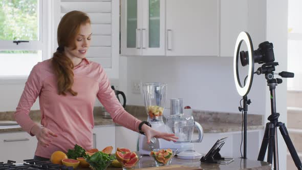 Woman chopping fruit and recording it with digital camera in the kitchen