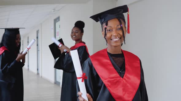 A Joyful Female Graduate with a Diploma in Hand Stands at the University Against the Background of