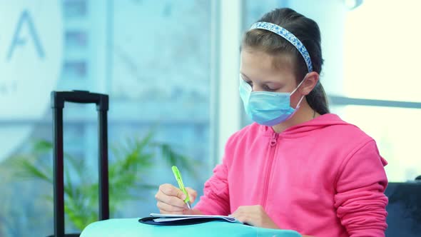 Portrait of a Girl, Kid in a Medical Mask, Drawing in a Notebook on a Suitcase, Luggage, at Airport