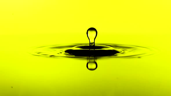 A Drop of Water Falls on the Surface of a Oil in Slow Motion. Yellow Background.
